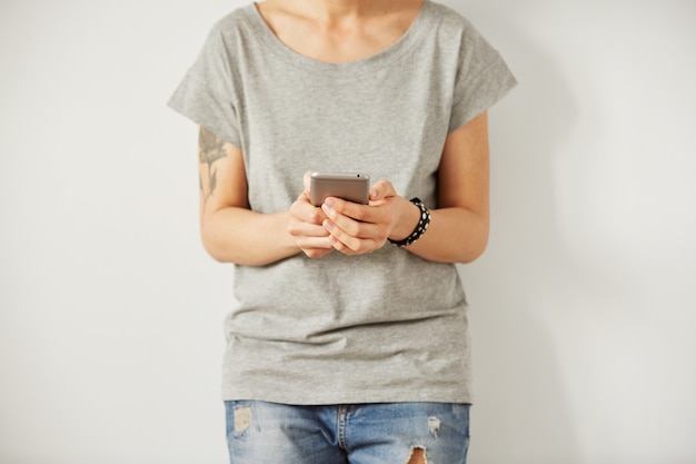 Donna bella hipster che controlla la posta elettronica tramite telefono cellulare mentre muro grigio