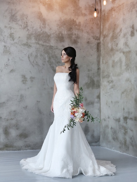 Donna bella sposa in abito da sposa che tiene un mazzo di fiori