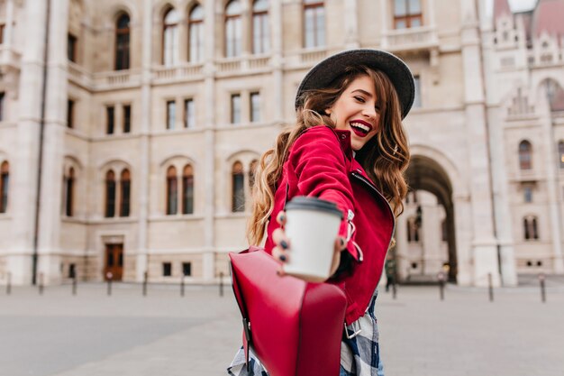 Donna bianca alla moda che posa con la tazza di latte sulla parete di architettura