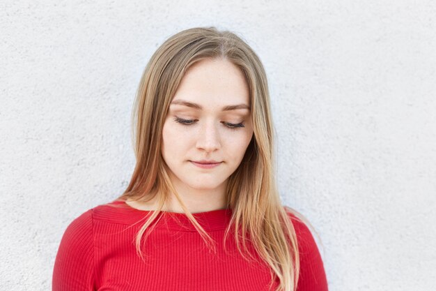 Donna bionda adorabile in vestito rosso che guarda meditatamente giù