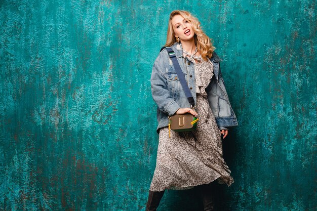 Donna bionda alla moda attraente sexy in jeans e giacca oversize che cammina contro il muro verde vintage in strada