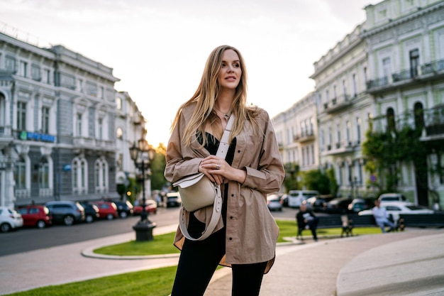 Donna bionda alla moda felice che posa sul viaggio di strada nell'ora legale dell'Europa