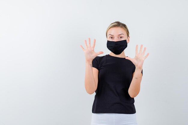 Donna bionda alzando le mani in gesto di resa in maglietta nera, pantaloni bianchi