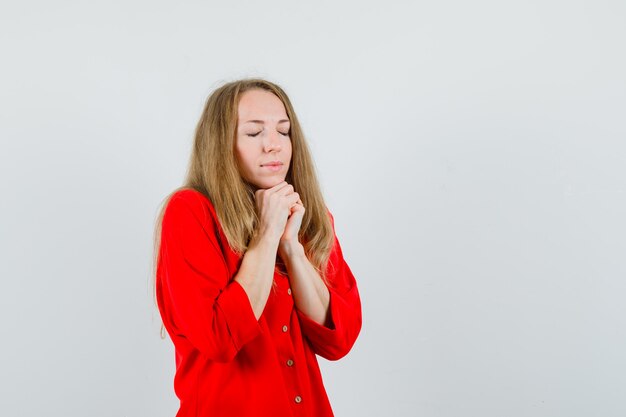 Donna bionda appoggiando il mento sulle mani giunte in camicia rossa e guardando speranzoso,