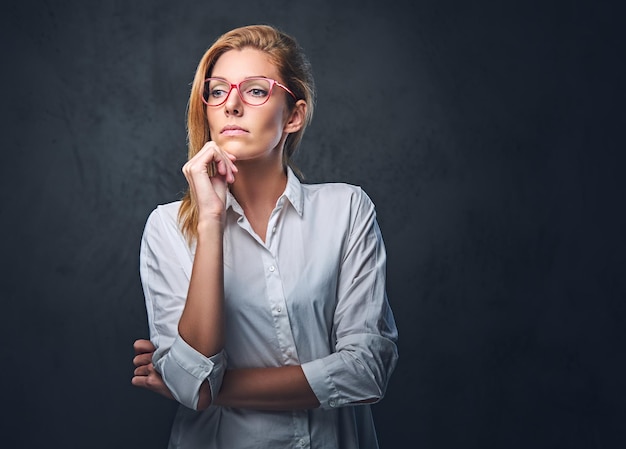 Donna bionda attraente di affari in una camicia bianca sopra fondo grigio.