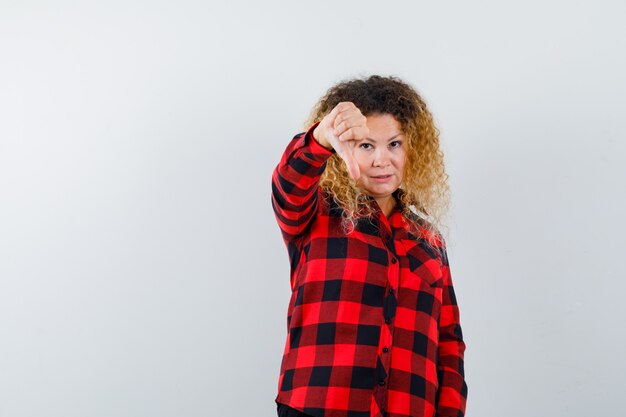 Donna bionda carina che mostra pollice in giù in camicia a quadri e sembra dispiaciuta. vista frontale.