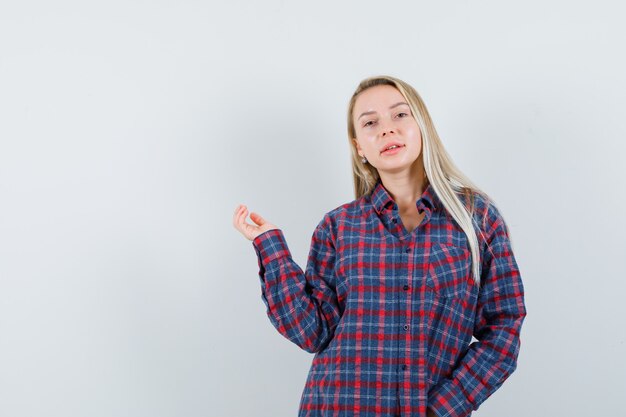 Donna bionda che allunga le mani e posa alla telecamera in camicia a quadri e sembra attraente. vista frontale.