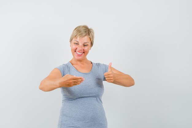 Donna bionda che finge di guardare il suo telefono e mostra come segno in maglietta azzurra e sembra allegra. vista frontale.