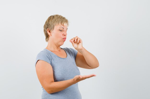 Donna bionda che finge di mangiare qualcosa e legge le notizie sul telefono in maglietta azzurra e sembra concentrata, vista frontale.