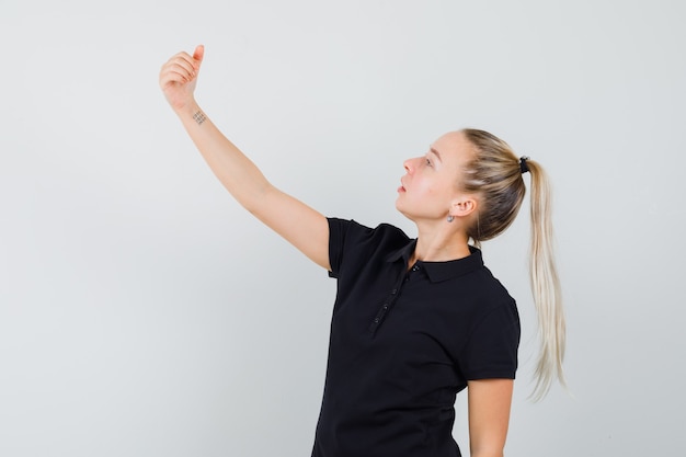 Donna bionda che finge di prendere selfie in maglietta nera e sembra ottimista