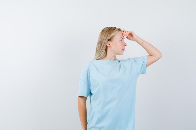 Donna bionda che guarda lontano con la mano sopra la testa in maglietta blu e sembra concentrata