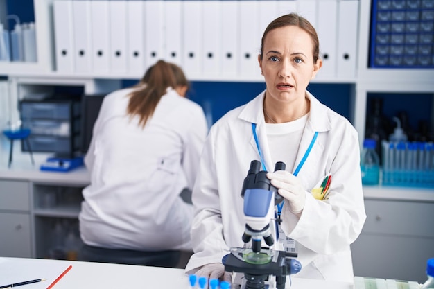 Donna bionda che lavora in un laboratorio privo di crudeltà spaventata e stupita con la bocca aperta per il viso incredulo a sorpresa