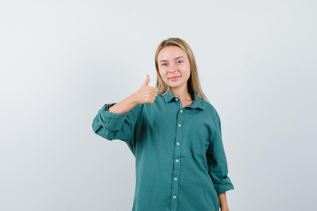 Donna bionda che mostra pollice in su in camicia verde e sembra allegra.