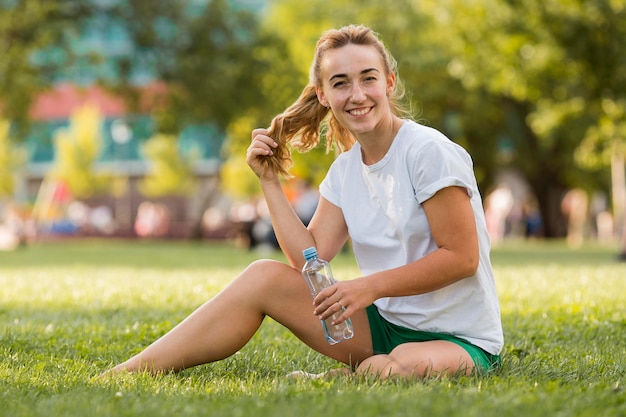 Donna bionda che si siede sull'erba in abiti sportivi