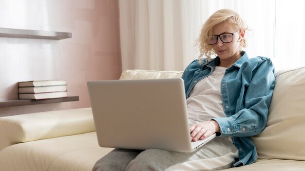 Donna bionda che si siede sullo strato e che lavora al computer portatile