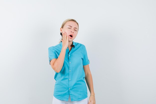 Donna bionda che soffre di mal di denti in camicetta blu e sembra dolorosa