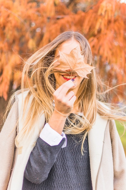 Donna bionda che sta sul vento con la foglia di autunno