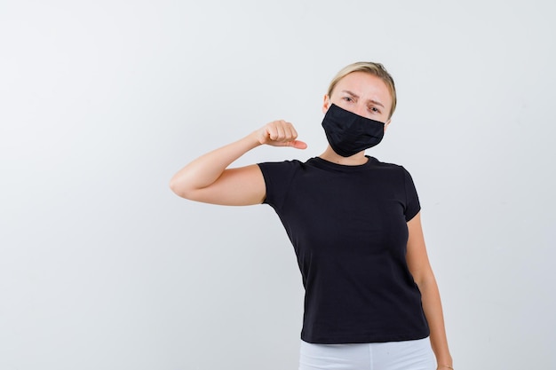 Donna bionda che stringe il pugno in maglietta nera, pantaloni bianchi, maschera nera e sembra seria