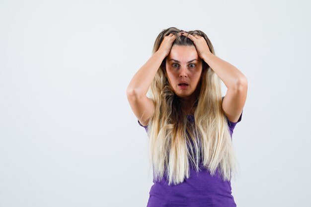 donna bionda che tiene le mani nei capelli in maglietta viola e guardando malinconico, vista frontale.