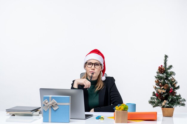 Donna bionda con un cappello di Babbo Natale seduto a un tavolo con un albero di Natale e un regalo