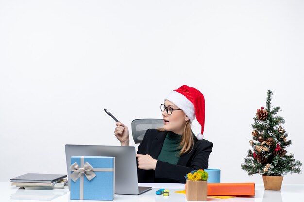 Donna bionda con un cappello di Babbo Natale seduto a un tavolo con un albero di Natale e un regalo