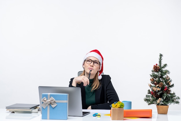 Donna bionda con un cappello di Babbo Natale seduto a un tavolo con un albero di Natale e un regalo