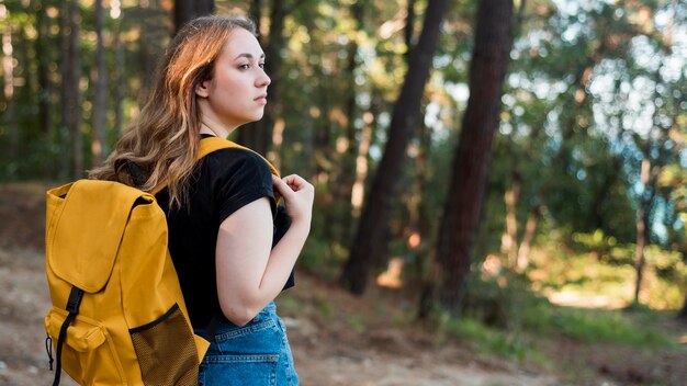 Donna bionda del colpo metà con lo zaino nella foresta