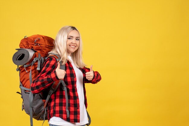 Donna bionda del viaggiatore di vista frontale con il suo zaino che dà i pollici in su