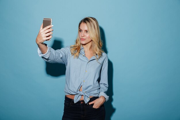 Donna bionda di bellezza in camicia che fa selfie sullo smartphone