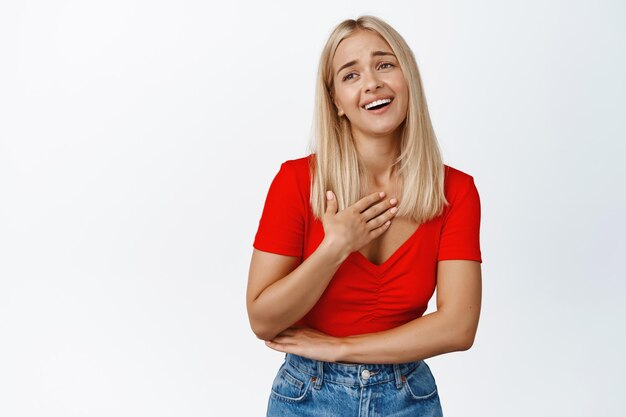 Donna bionda felice che ride sorridente e che sembra grata soddisfatta di qualcosa in piedi su sfondo bianco