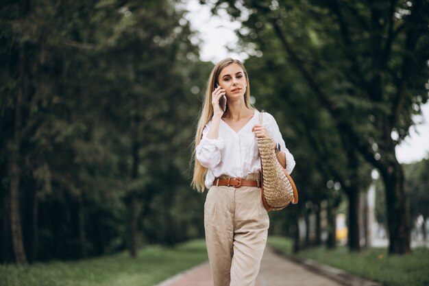 Donna bionda graziosa che utilizza telefono fuori nel parco