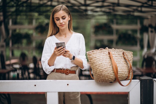 Donna bionda graziosa che utilizza telefono fuori nel parco