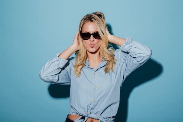 Donna bionda graziosa in camicia ed occhiali da sole che esaminano macchina fotografica