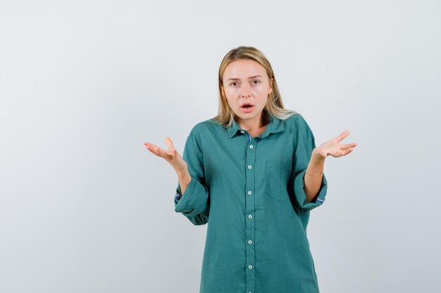 Donna bionda in camicia verde che mostra un gesto impotente e sembra perplessa