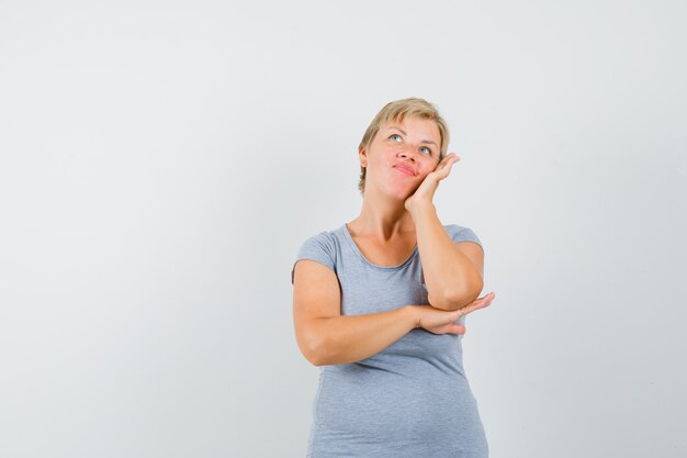 Donna bionda in maglietta azzurra che finge di guardare il suo telefono e sembra sorpresa, vista frontale.