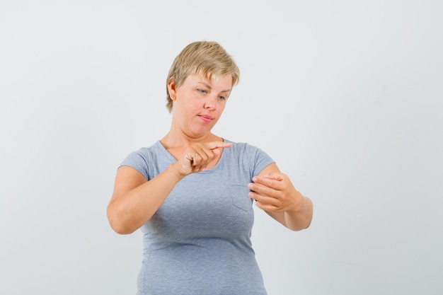 Donna bionda in maglietta azzurra che finge di leggere qualcosa sul telefono e che sembra concentrata, vista frontale.