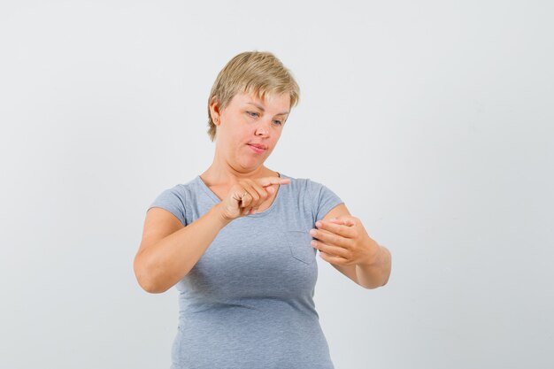 Donna bionda in maglietta azzurra che finge di leggere qualcosa sul telefono e che sembra concentrata, vista frontale.