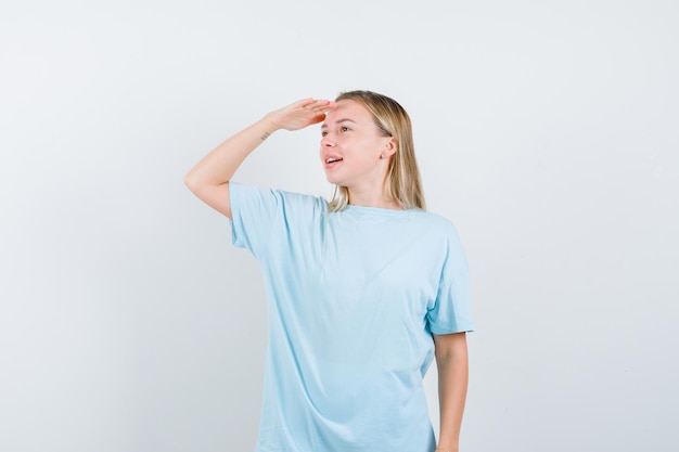 Donna bionda in maglietta blu che guarda lontano con la mano sopra la testa e sembra concentrata