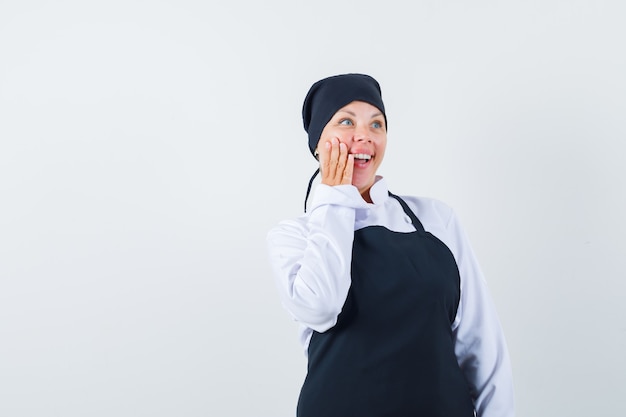 Donna bionda in uniforme nera del cuoco che mette la mano sulla guancia e che sembra sorpresa