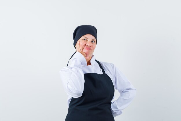 Donna bionda in uniforme nera del cuoco che tiene il dito indice vicino alla bocca e che sembra pensieroso