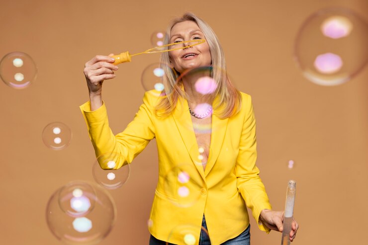 Foto gratuito donna bionda senior che soffia bolle su uno sfondo giallo