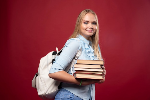 Donna bionda studentessa in possesso di una pila di libri e sembra positiva.