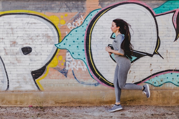 Donna bruna che corre contro il muro di cemento