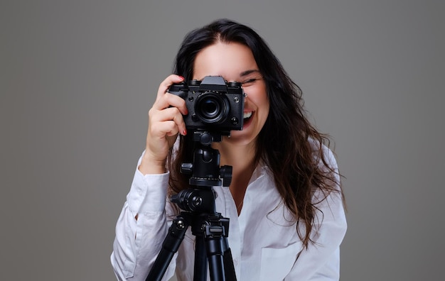 Donna bruna sorridente e positiva con gli occhiali che scatta foto con una macchina fotografica professionale. Isolato su sfondo grigio.