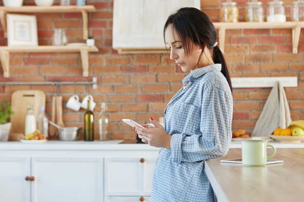 Donna bruna vestita casualmente, ha unghie dipinte, guarda seriamente lo smart phone