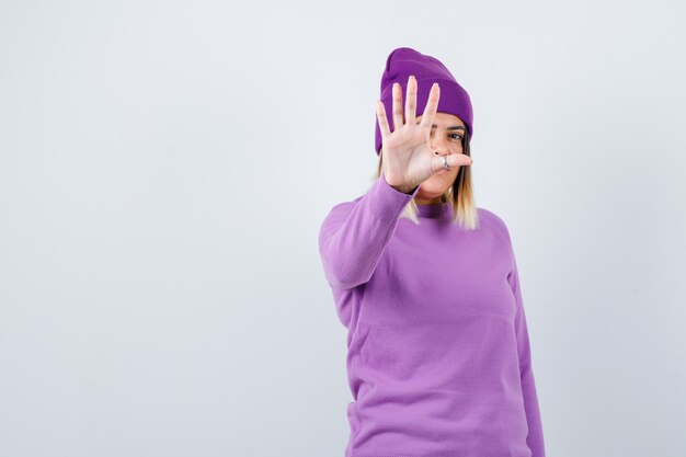 Donna carina che mostra il gesto di arresto in maglione, berretto e sembra risoluta. vista frontale.