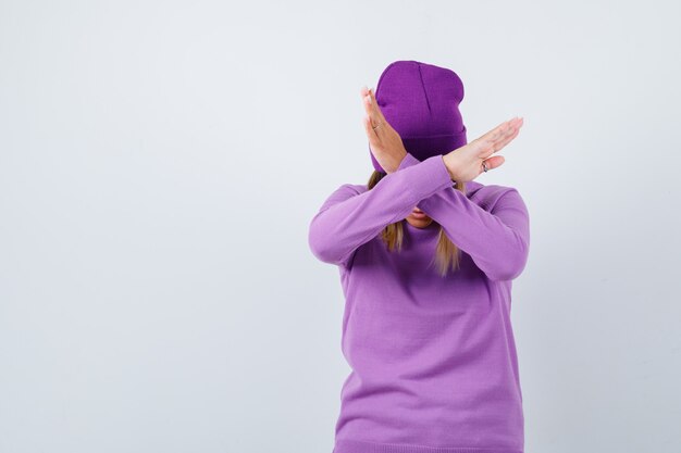 Donna carina in maglione, berretto che mostra gesto di rifiuto e sembra risoluta, vista frontale.