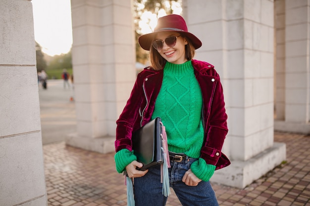 Donna carina in stile autunnale vestito alla moda che cammina per strada indossando giacca di velluto viola, occhiali da sole e cappello