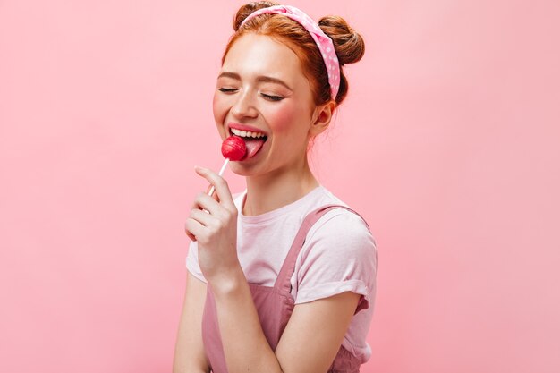 Donna carina rossa in abito bianco e top lecca lecca-lecca su sfondo rosa.