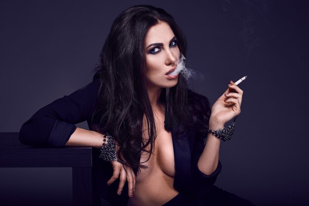 Donna castana calda elegante che fuma una sigaretta